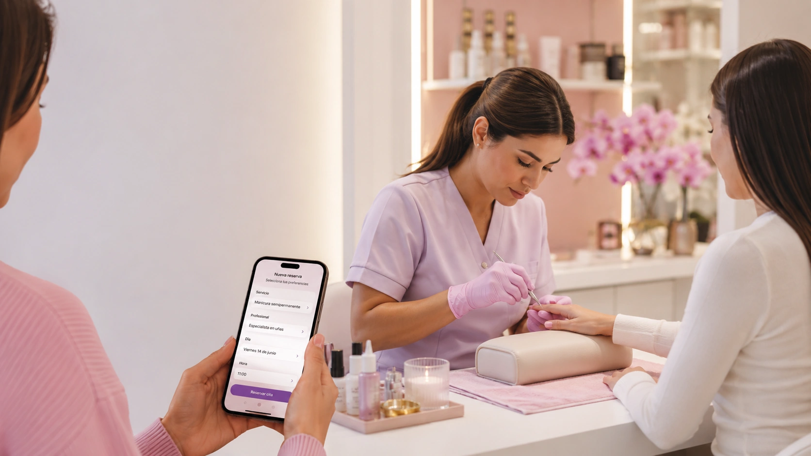 Especialista realizando una manicura mientras otra clienta reserva online desde el móvil